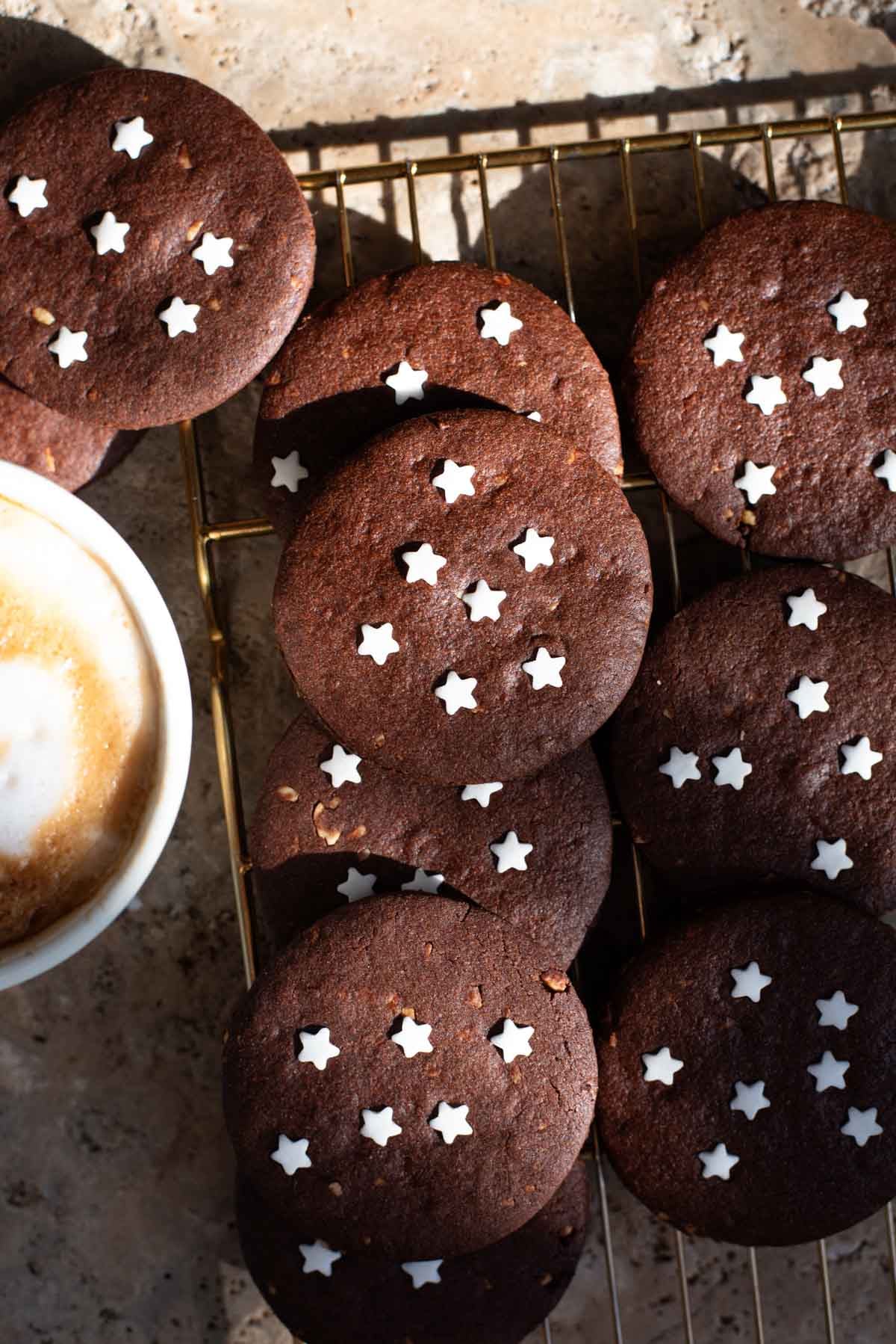 An overhead shot of lots of Pan di Stelle Italian cookies on a cooling rack with a cappuccino at the side.
