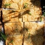 An overhead shot showing an Italian potato flatbread cut into 8 slices on a rustic wooden board topped with rosemary.