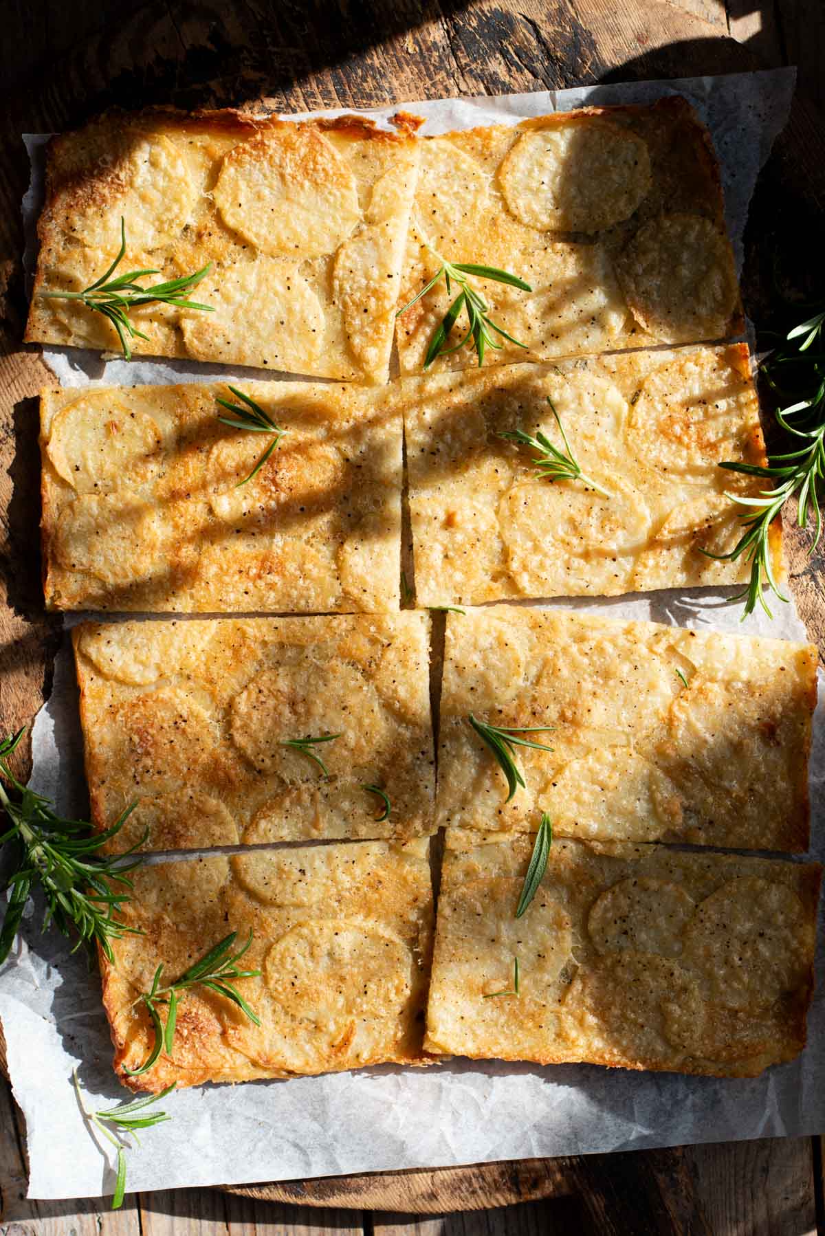 An overhead shot of an Italian potato flatbread cut into 8 slices topped with rosemary.