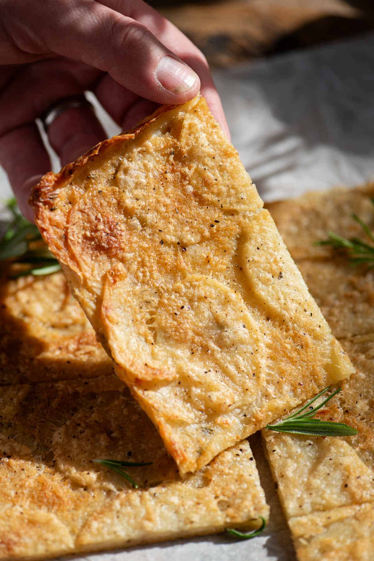 A close up of a hand holding a slice of potato flatbread.