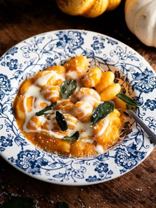 Gnocchi with a butternut squash sauce and taleggio cream topped with crispy sage. The bowl is blue floral and the background is rustic wood.