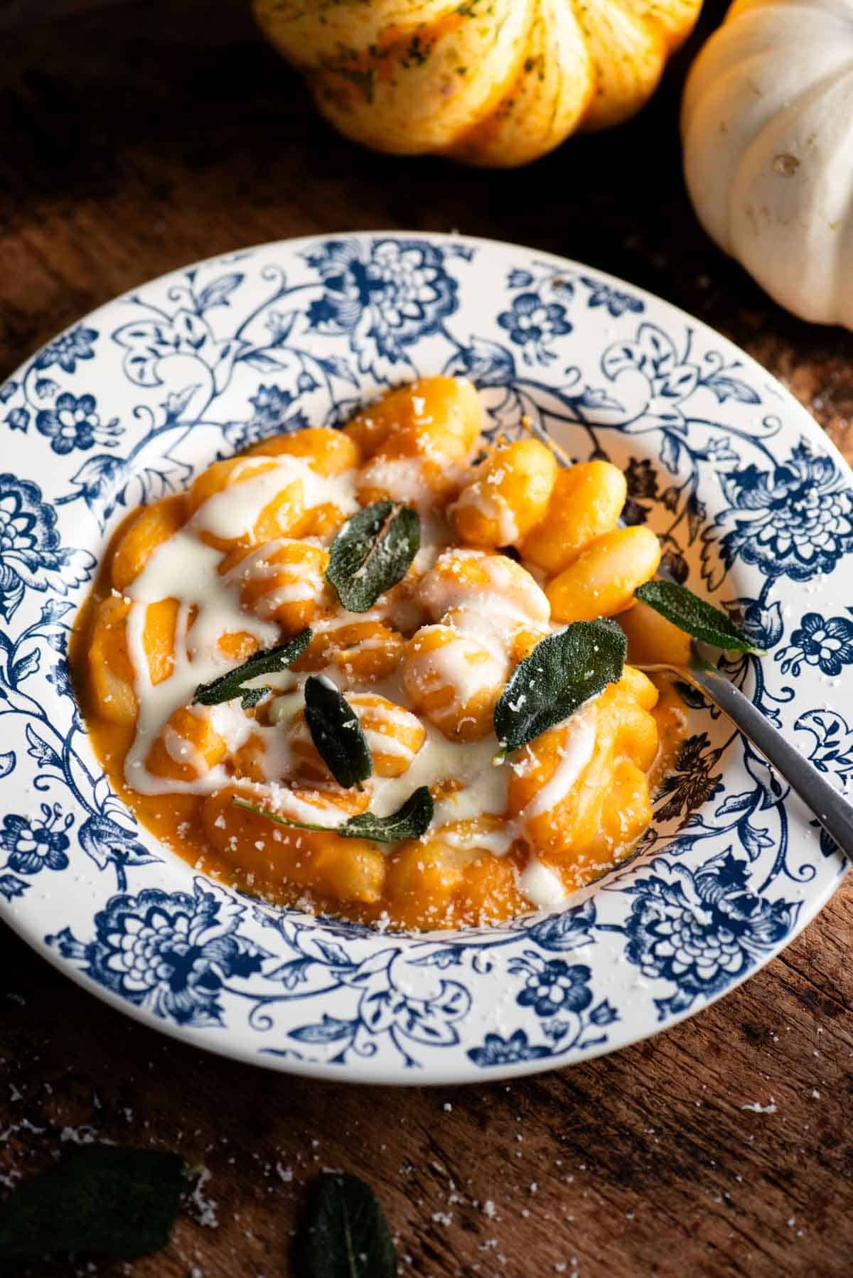 Gnocchi with a butternut squash sauce and taleggio cream topped with crispy sage. The bowl is blue floral and the background is rustic wood.