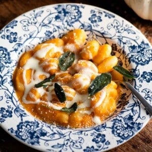 A close up cropped image of butternut squash gnocchi in a blue floral bowl topped with taleggio cream and sage leaves.