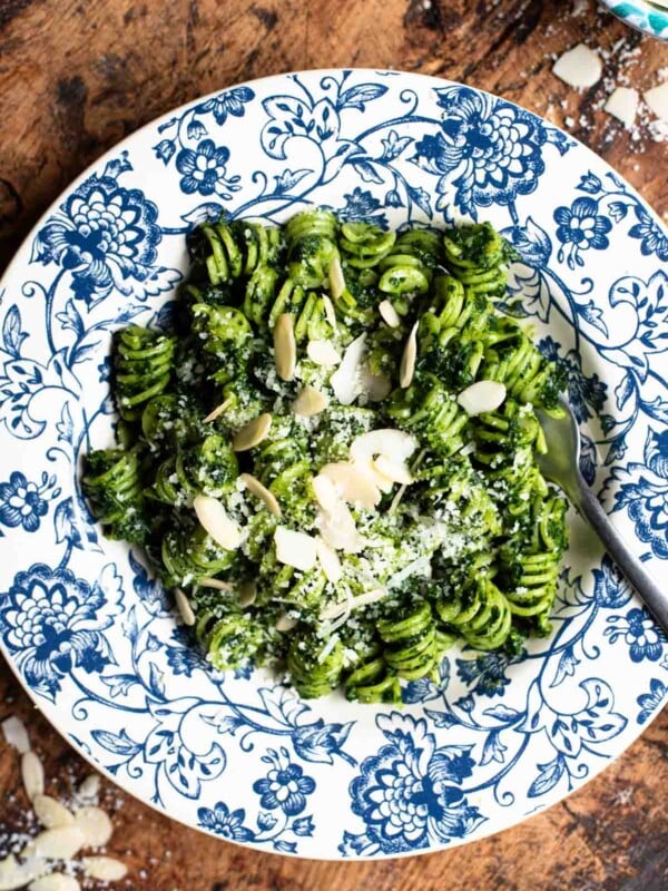 An overhead shot of pasta with kale pesto in a blue floral bowl on a rustic wooden surface.