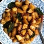 An overhead shot of crispy pan-fried potatoes with pancetta and sage in a blue and white vintage style bowl.