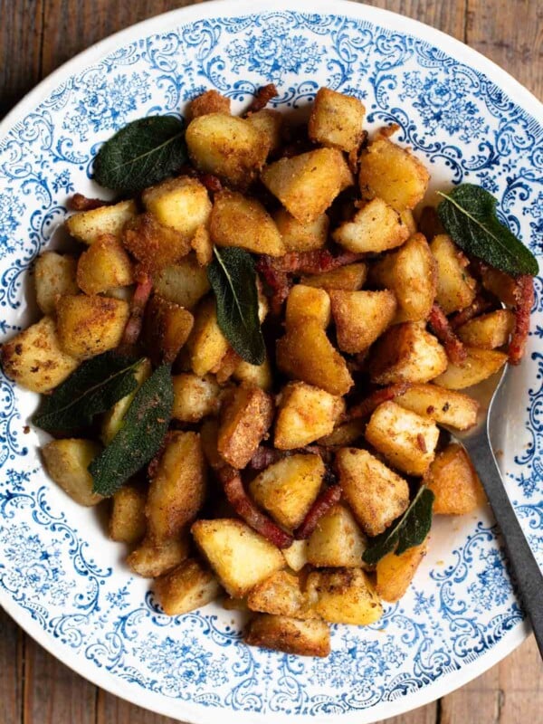 Crispy pan-fried potatoes with pancetta and sage in a blue and white patterned bowl on a rustic wooden surface.
