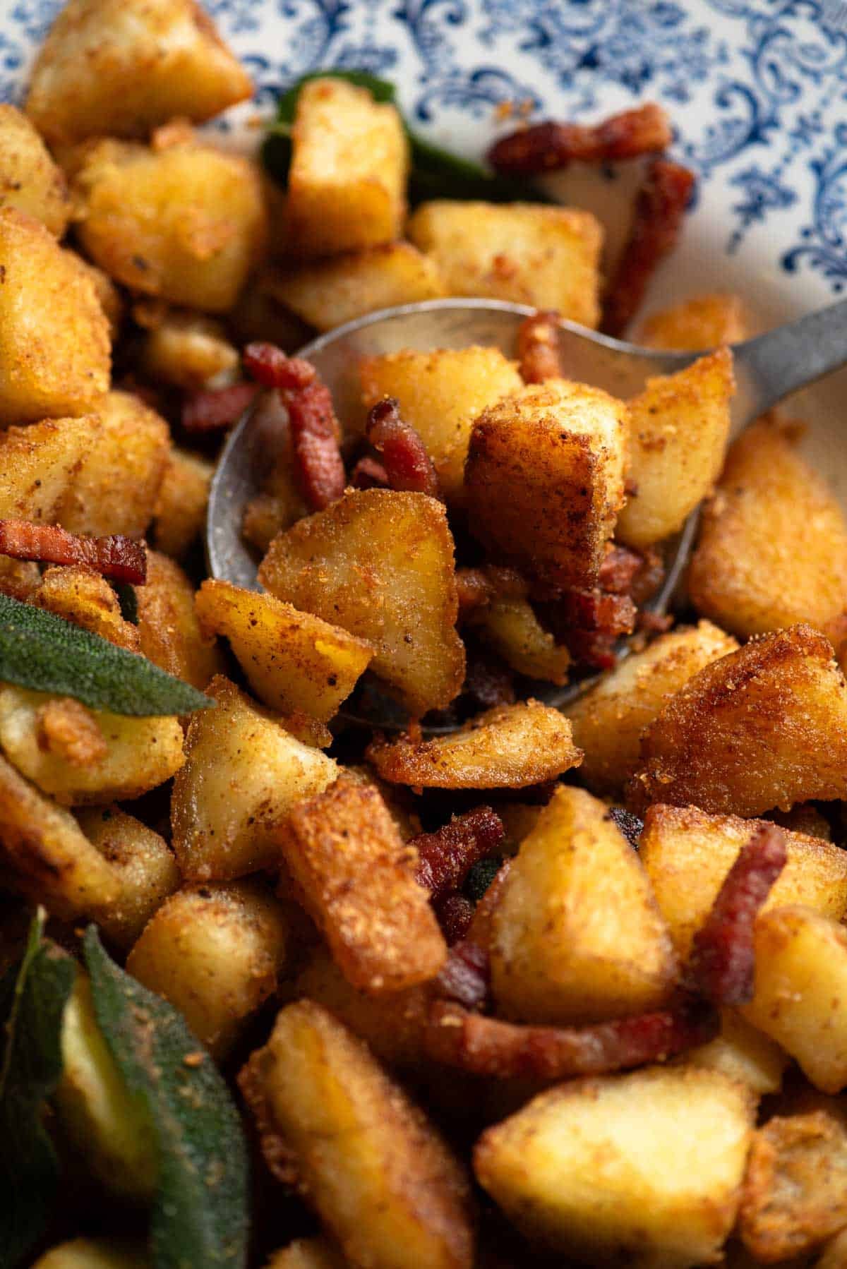 A close up of a spoon in a bowl of crispy potatoes with pancetta and sage.