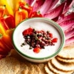 A side shot of a tuna dip in a small serving bowl with peppers and chicory leaves at the side.